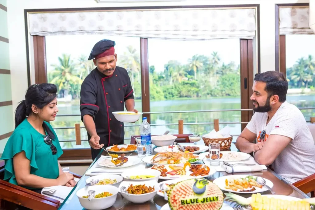 Chef serving a Kerala meal to a couple on a Lake Queen houseboat in Alleppey